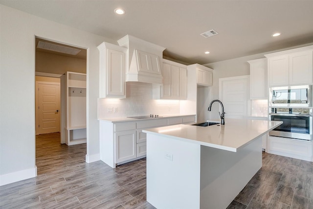 kitchen featuring a center island with sink, white cabinets, sink, light wood-type flooring, and wall oven