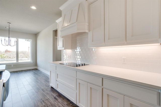 kitchen with tasteful backsplash, black electric cooktop, white cabinetry, and premium range hood