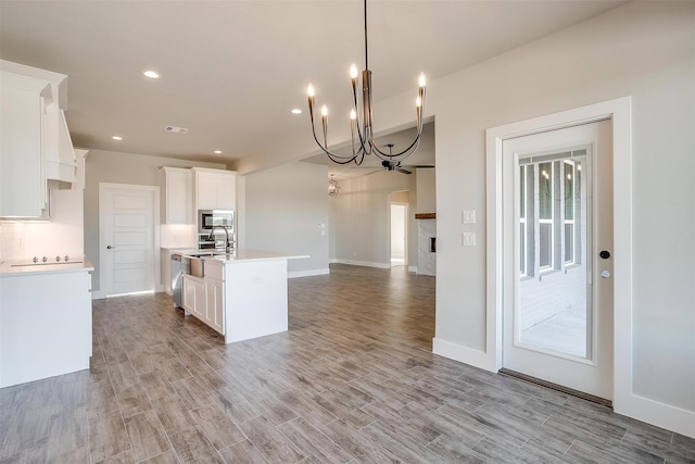 kitchen with a kitchen island with sink, decorative light fixtures, a notable chandelier, light hardwood / wood-style floors, and white cabinetry