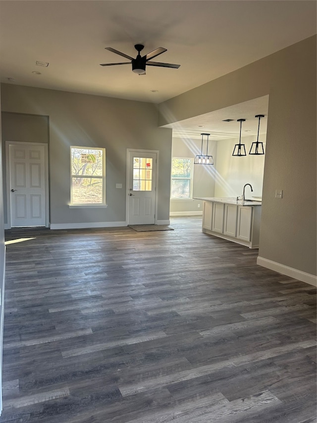 unfurnished living room featuring dark wood-type flooring, ceiling fan, a healthy amount of sunlight, and sink