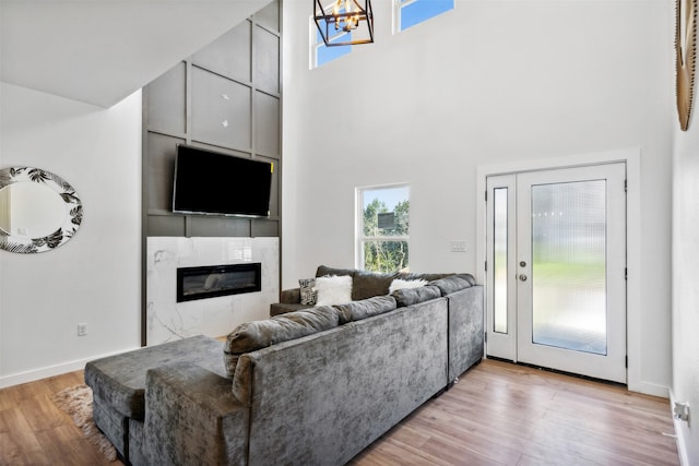 living room with a high ceiling, a tiled fireplace, a notable chandelier, and light hardwood / wood-style floors