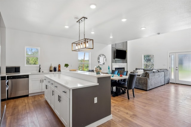 kitchen featuring stainless steel appliances, a kitchen island, pendant lighting, light wood-type flooring, and white cabinetry