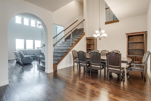 dining space with dark hardwood / wood-style flooring, a towering ceiling, and a chandelier