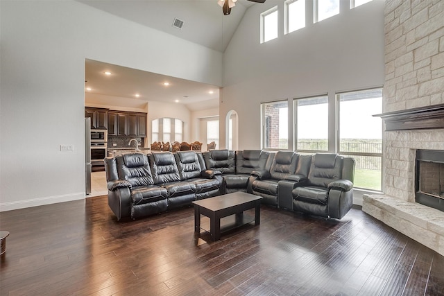 living room with ceiling fan, sink, dark wood-type flooring, high vaulted ceiling, and a fireplace