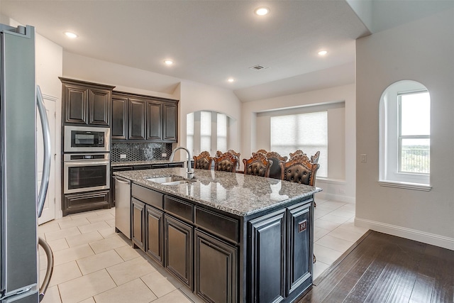 kitchen with a center island with sink, sink, decorative backsplash, light stone countertops, and appliances with stainless steel finishes