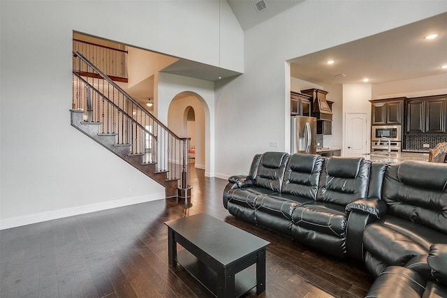 living area with visible vents, baseboards, a towering ceiling, dark wood-type flooring, and stairs