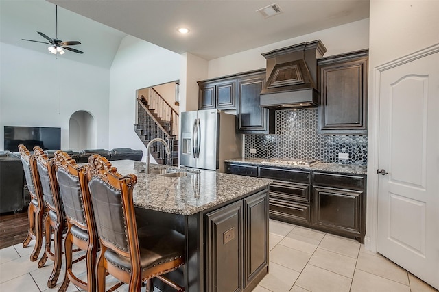 kitchen featuring premium range hood, a kitchen island with sink, sink, a breakfast bar area, and stainless steel appliances