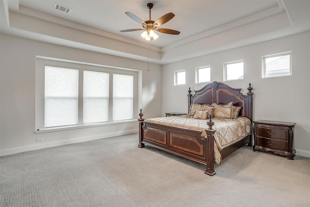 bedroom featuring a tray ceiling, light colored carpet, visible vents, a ceiling fan, and baseboards