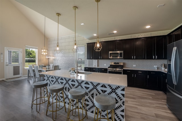 kitchen featuring stainless steel appliances, backsplash, decorative light fixtures, sink, and light hardwood / wood-style flooring