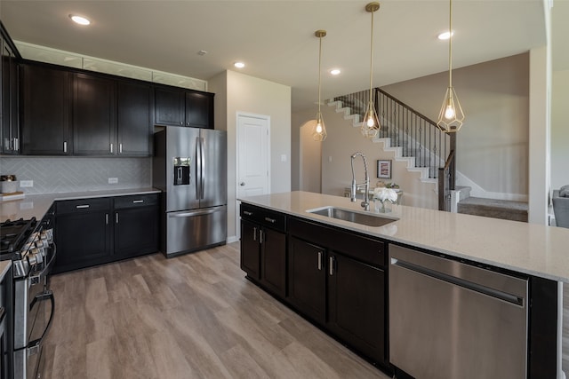 kitchen featuring stainless steel appliances, sink, light stone countertops, light wood-type flooring, and decorative light fixtures