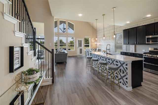 kitchen with stainless steel appliances, decorative light fixtures, hardwood / wood-style floors, a breakfast bar, and a kitchen island with sink