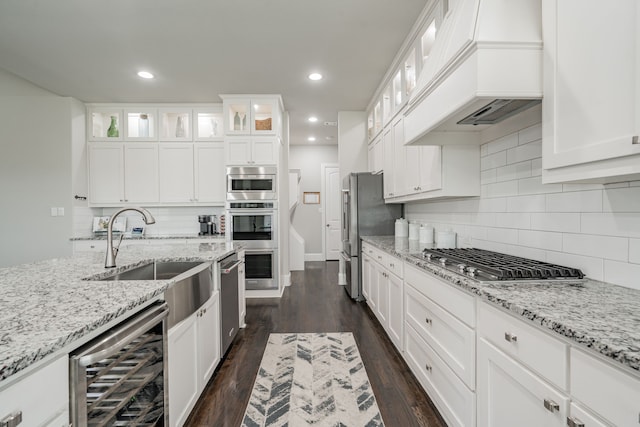 kitchen with stainless steel appliances, beverage cooler, light stone counters, premium range hood, and white cabinets