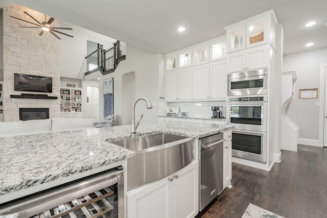 kitchen featuring sink, beverage cooler, a stone fireplace, white cabinets, and appliances with stainless steel finishes