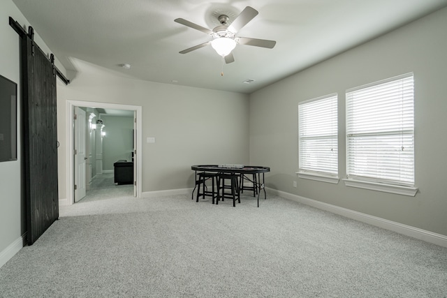 dining area featuring a barn door, ceiling fan, and light colored carpet