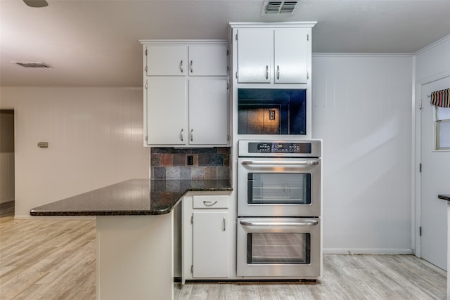 kitchen featuring white cabinetry, kitchen peninsula, backsplash, stainless steel double oven, and light wood-type flooring