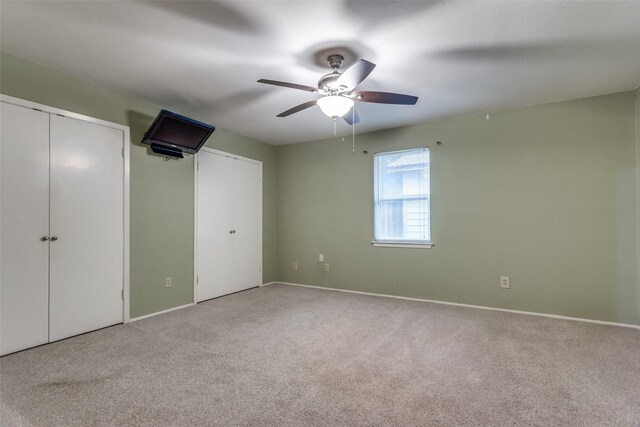 unfurnished bedroom with two closets, baseboards, a ceiling fan, and carpet floors