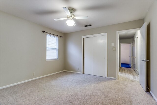 unfurnished bedroom featuring light colored carpet, a closet, baseboards, visible vents, and a ceiling fan