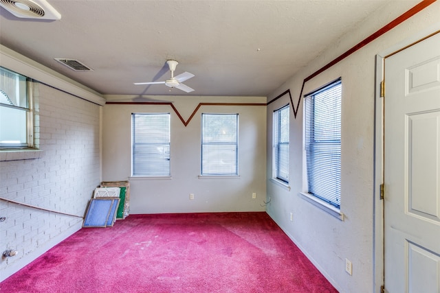 carpeted spare room featuring a textured ceiling, brick wall, and ceiling fan