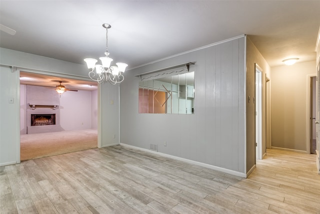 unfurnished dining area with a fireplace, ceiling fan with notable chandelier, wooden walls, and light hardwood / wood-style flooring