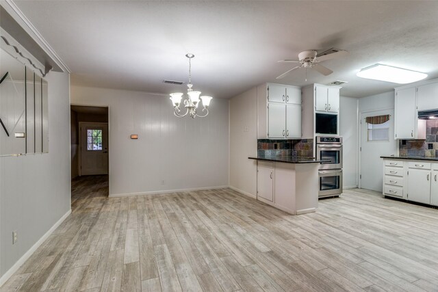 kitchen with tasteful backsplash, light wood-style flooring, double oven, dark countertops, and ceiling fan with notable chandelier