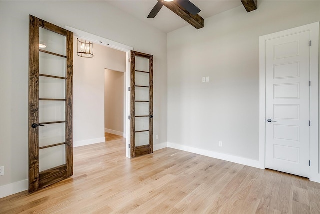 spare room featuring beam ceiling, baseboards, light wood finished floors, and ceiling fan