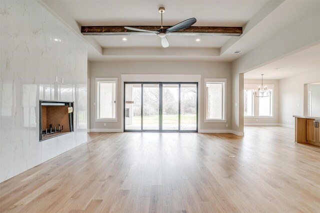 unfurnished living room with a premium fireplace, beam ceiling, baseboards, and light wood finished floors