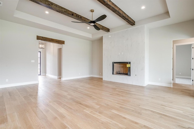 unfurnished living room featuring a high end fireplace, beam ceiling, baseboards, and light wood-style floors