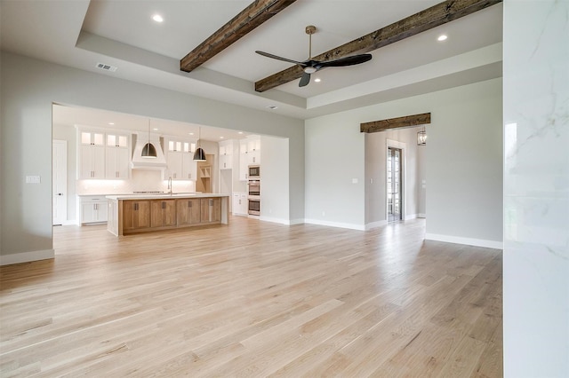 unfurnished living room featuring beam ceiling, baseboards, visible vents, and light wood-type flooring