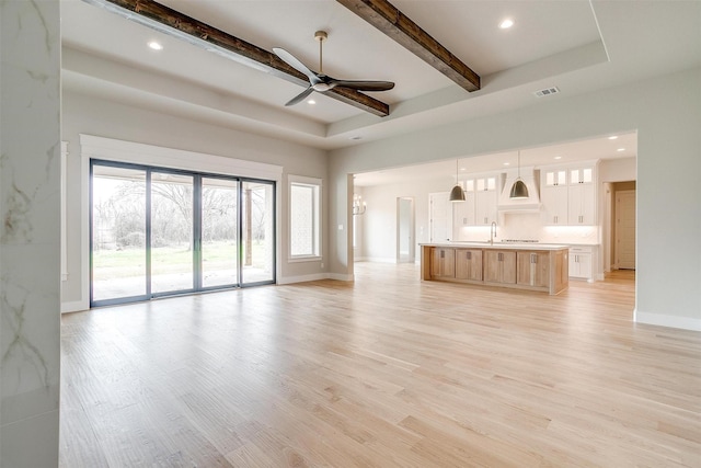 unfurnished living room featuring visible vents, beamed ceiling, light wood-style flooring, ceiling fan with notable chandelier, and baseboards