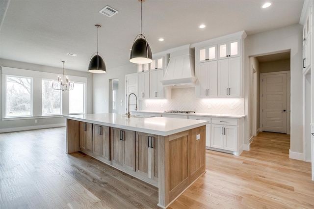 kitchen featuring visible vents, backsplash, a sink, custom exhaust hood, and a kitchen island with sink