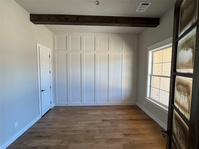 unfurnished bedroom with beamed ceiling and dark wood-type flooring