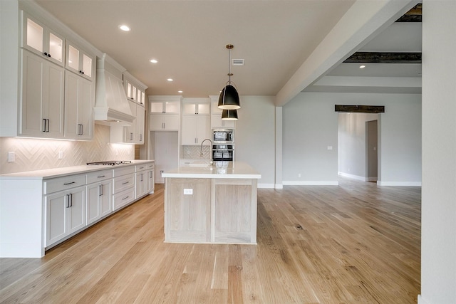 kitchen with custom exhaust hood, light countertops, light wood-style floors, appliances with stainless steel finishes, and tasteful backsplash