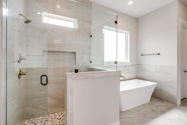 bathroom with tile walls, a freestanding bath, a healthy amount of sunlight, and a stall shower