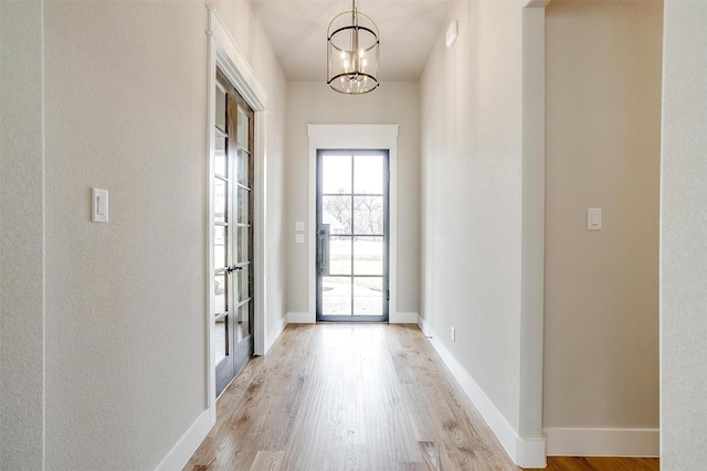 entryway featuring baseboards, light wood-style floors, and an inviting chandelier