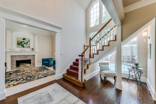 staircase featuring ornamental molding, a towering ceiling, a tiled fireplace, and hardwood / wood-style flooring