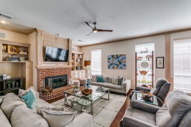 living room featuring ornamental molding, light hardwood / wood-style floors, a healthy amount of sunlight, and a brick fireplace