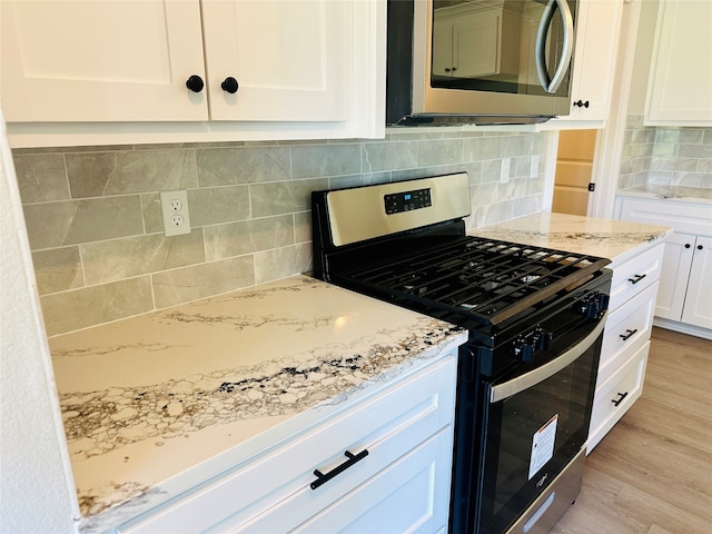 kitchen with appliances with stainless steel finishes, light stone countertops, backsplash, light hardwood / wood-style flooring, and white cabinets