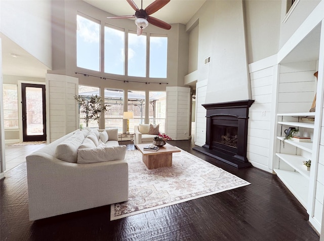 living room featuring plenty of natural light, visible vents, dark wood finished floors, and a fireplace with raised hearth