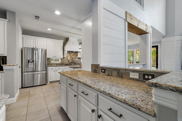 kitchen featuring light tile patterned floors, visible vents, decorative backsplash, stainless steel fridge with ice dispenser, and premium range hood