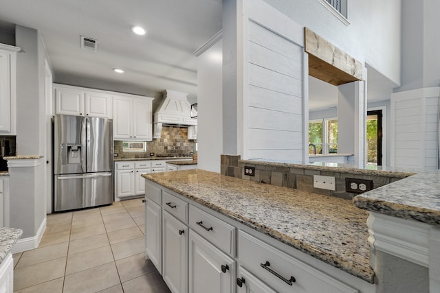 kitchen featuring white cabinetry, custom range hood, stainless steel fridge with ice dispenser, and light stone counters