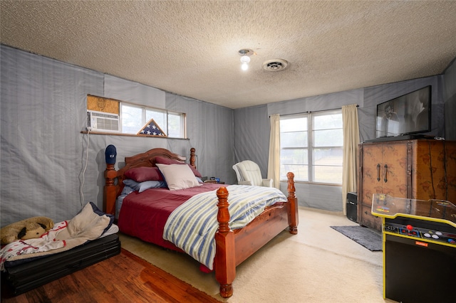 carpeted bedroom featuring a textured ceiling, a wall unit AC, and multiple windows