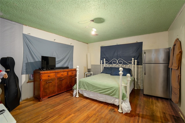 bedroom featuring dark wood-type flooring, stainless steel fridge, and a textured ceiling