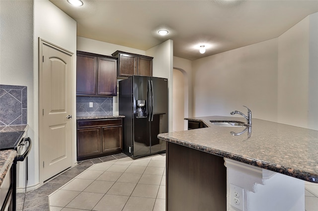 kitchen featuring sink, black refrigerator with ice dispenser, light tile patterned floors, dark brown cabinets, and decorative backsplash