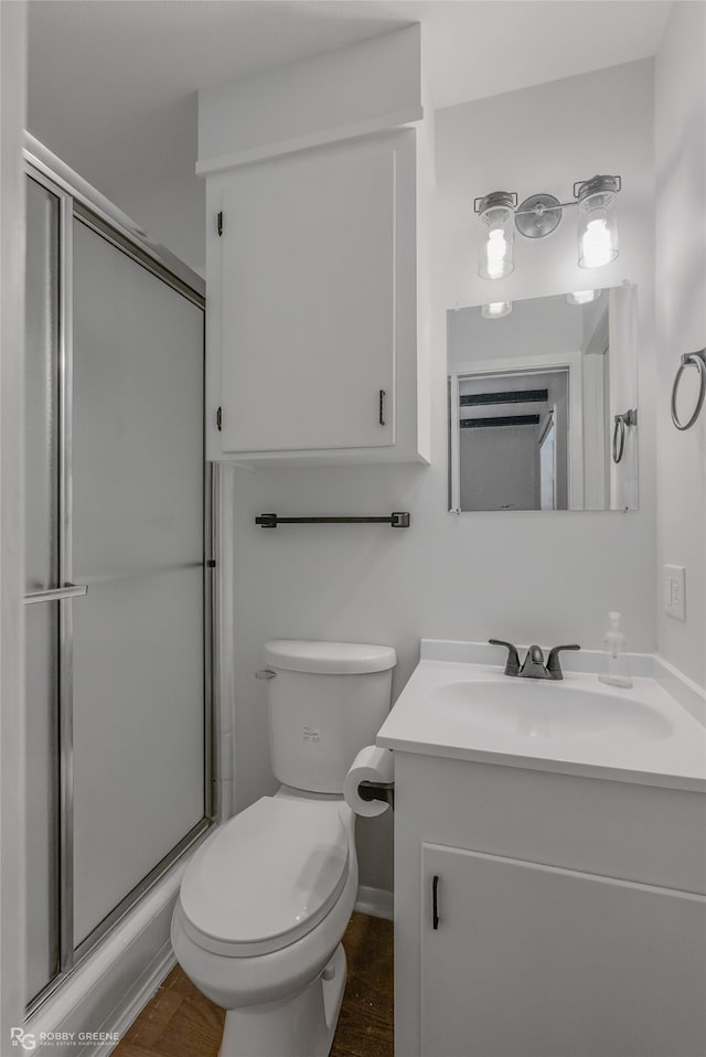 bathroom with hardwood / wood-style flooring, a shower with shower door, vanity, and toilet