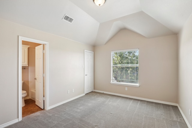 unfurnished bedroom with carpet, ensuite bathroom, a closet, and vaulted ceiling