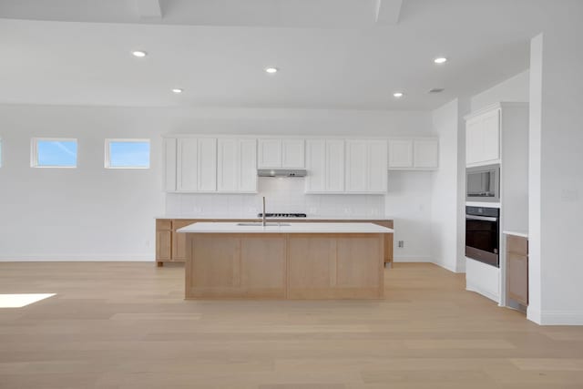 kitchen with decorative backsplash, black oven, white cabinets, and a center island with sink