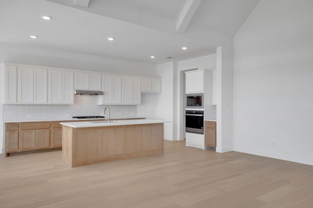 kitchen featuring sink, tasteful backsplash, light hardwood / wood-style floors, a center island with sink, and white cabinets