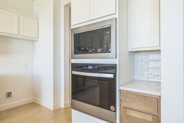 kitchen with stainless steel gas stovetop, decorative backsplash, light wood-type flooring, range hood, and white cabinetry