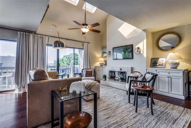 living room featuring vaulted ceiling with skylight, ceiling fan, and dark wood-type flooring