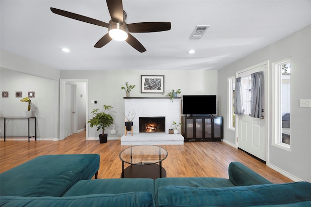 living room with a fireplace, ceiling fan, and light wood-type flooring